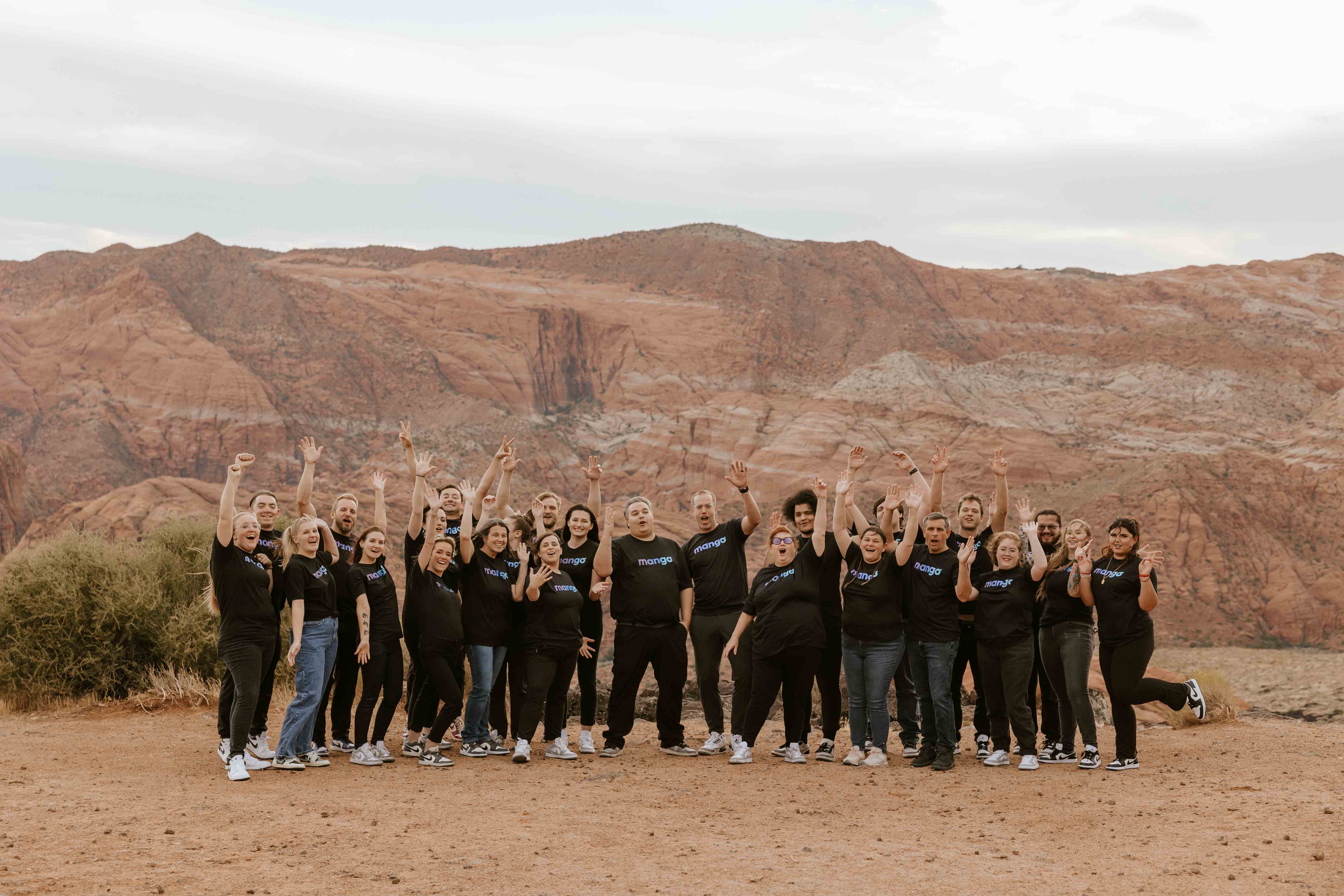 The Mango Voice team cheering together in front of the red rock mountains of southern Utah