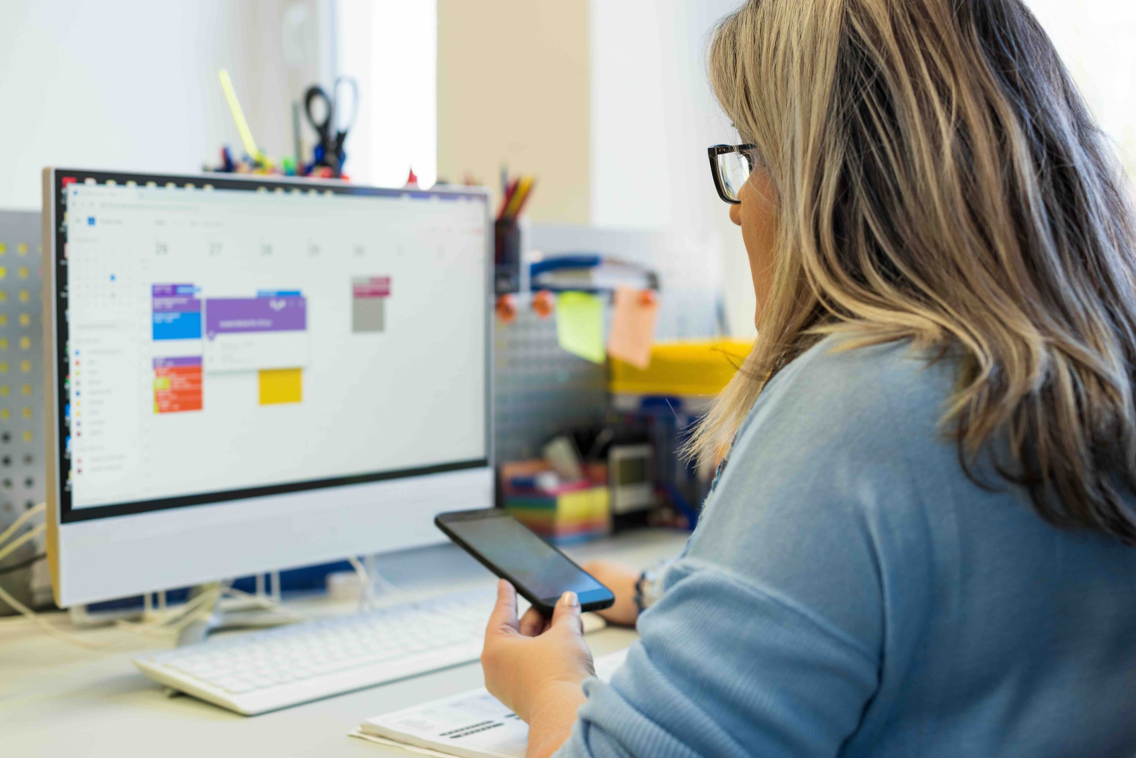 Front desk team member on a phone call while viewing the practice scheduling calendar on a desktop monitor