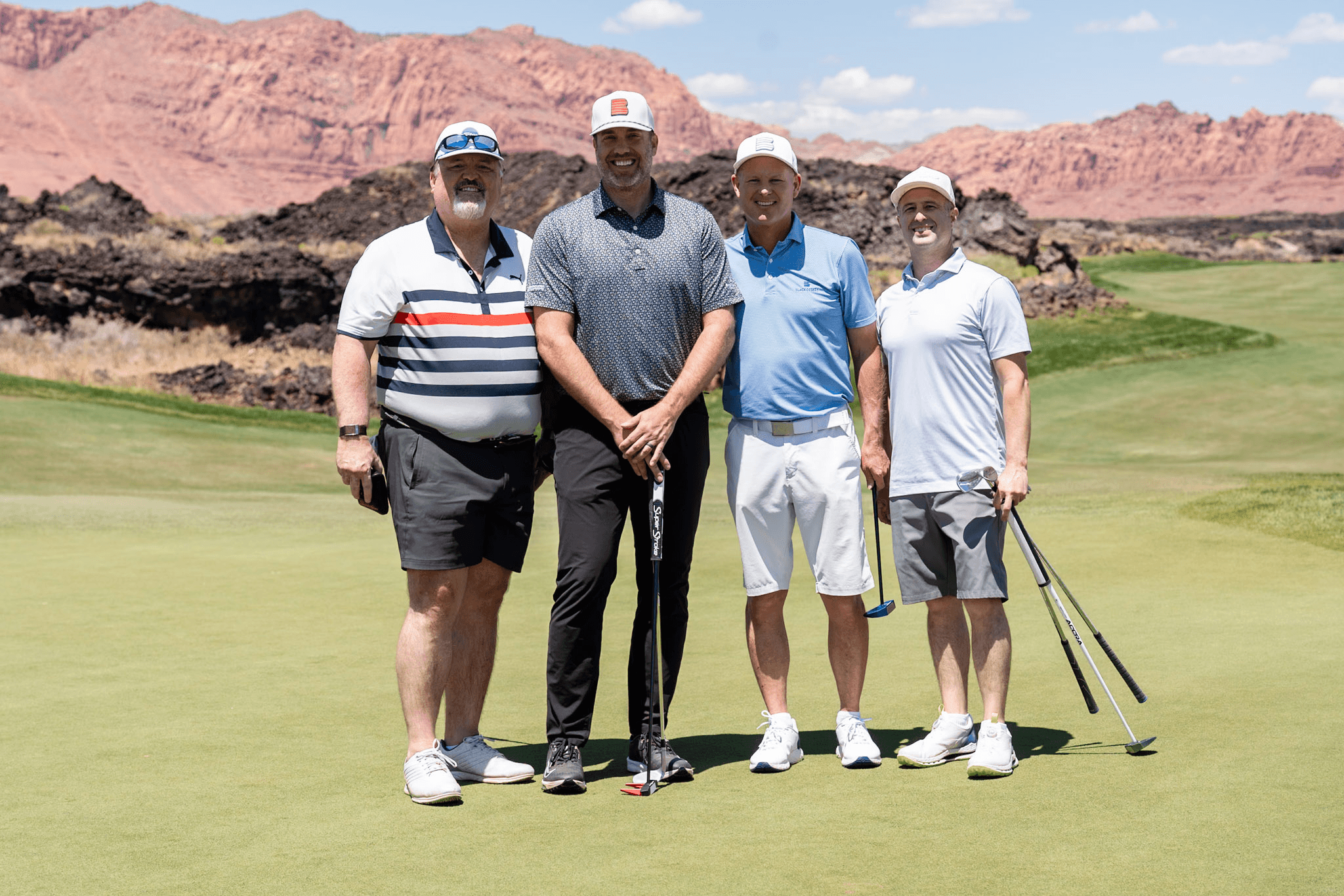 Four golfers posing on the green with red rock cliffs behind them