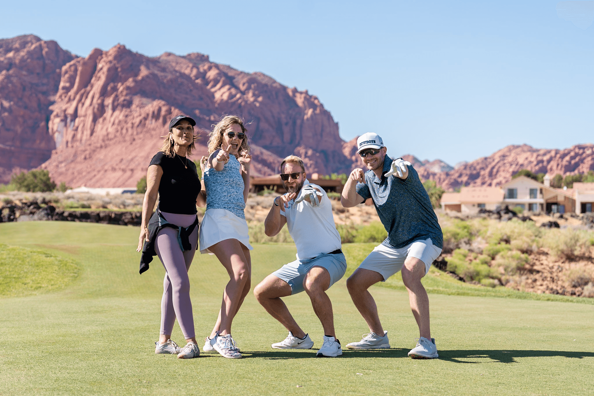 Four golfers posing playfully in front of red rock cliffs at the Mango Open