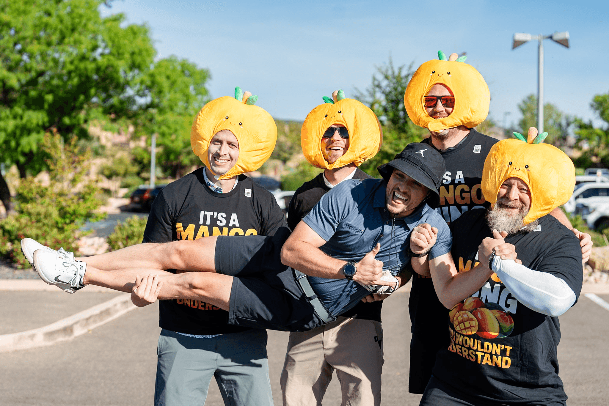 Group of golfers wearing plush mango hats and lifting a friend, laughing