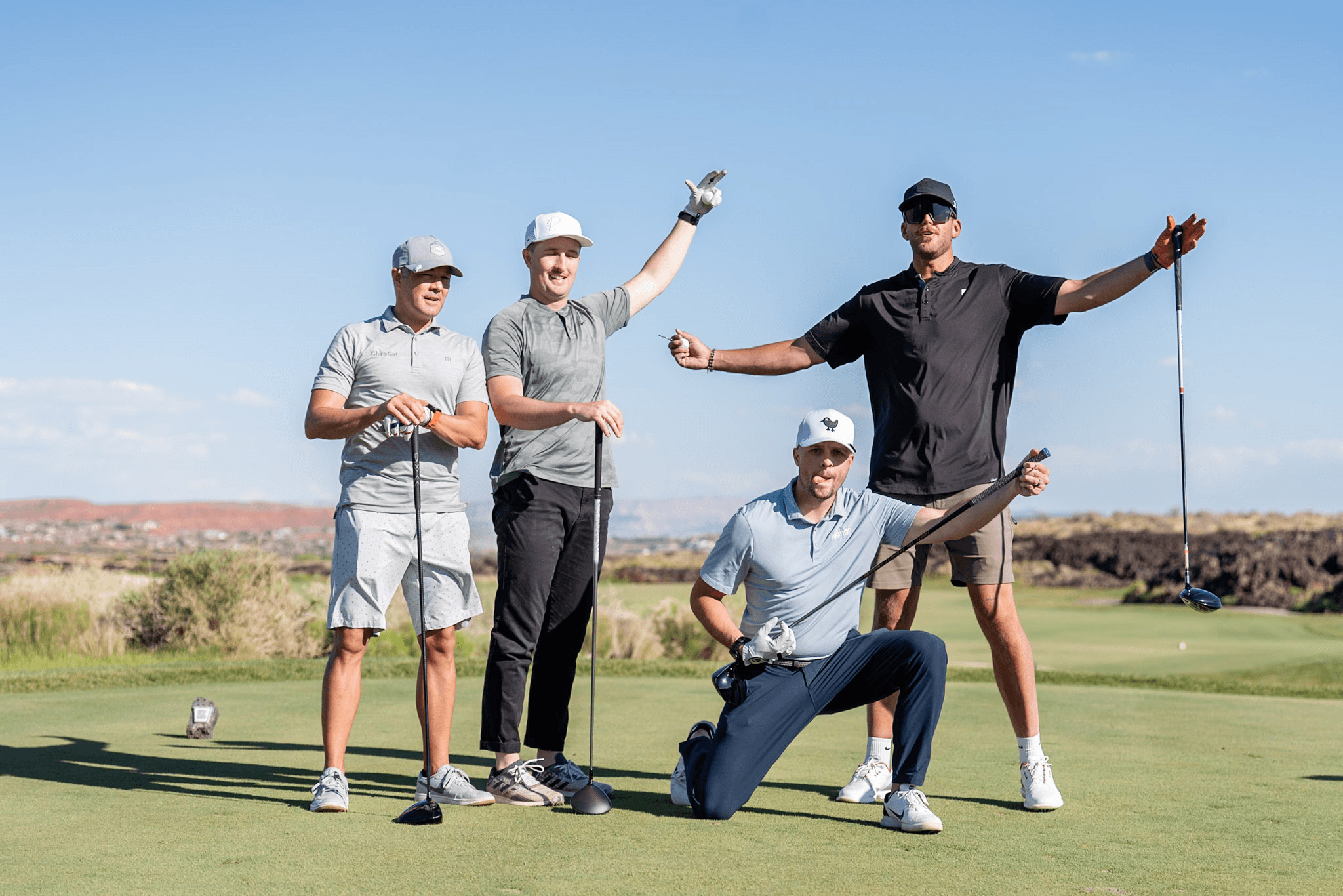 Four golfers posing energetically on a tee box with a desert vista