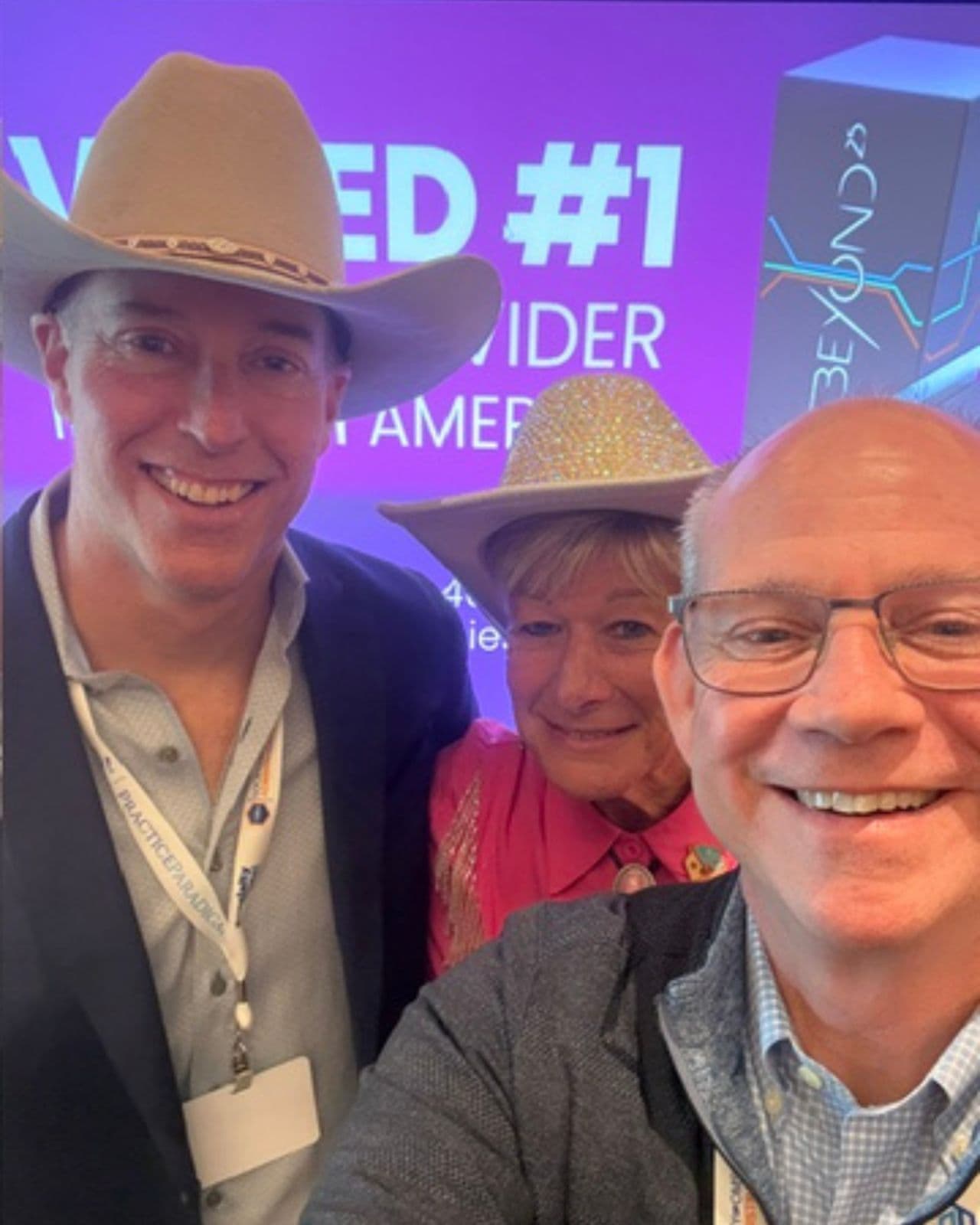 Three attendees, two wearing cowboy hats, smiling together at a dental industry event